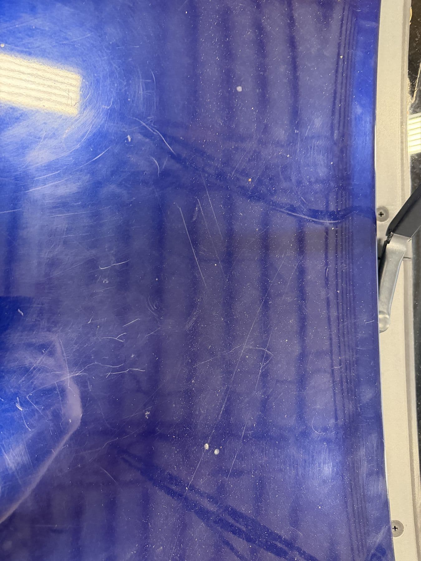 Blue paint under an inspection light showing swirl marks and wash scratches before paint correction