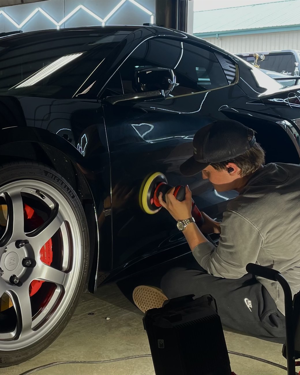 Technician machine-polishing a black Corvette's panel with a dual-action polisher at Albrecht Auto Spa